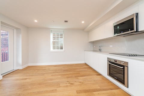 a white kitchen with a wooden floor and a stove and a television
